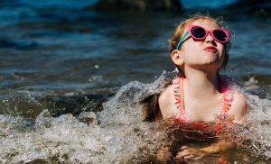 Small child in goggles bursting up out of a wave