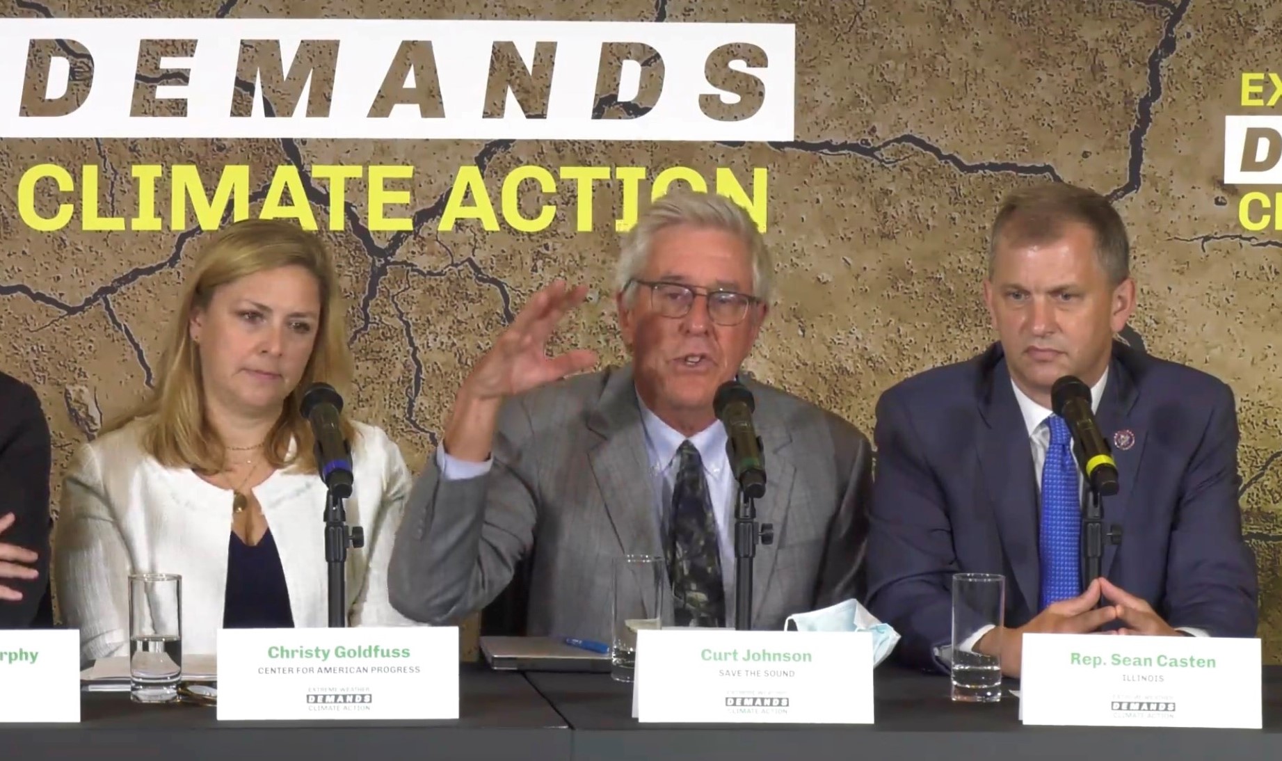 Save the Sound president Curt Johnson, flanked by two people, gesticulating in front of a sign that says "demands climate action"